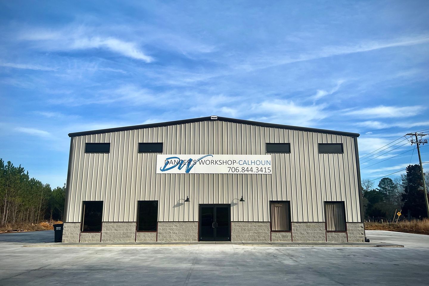 A tan metal studio building with a Dancer's Workshop Calhoun sign and glass front doors under a blue sky